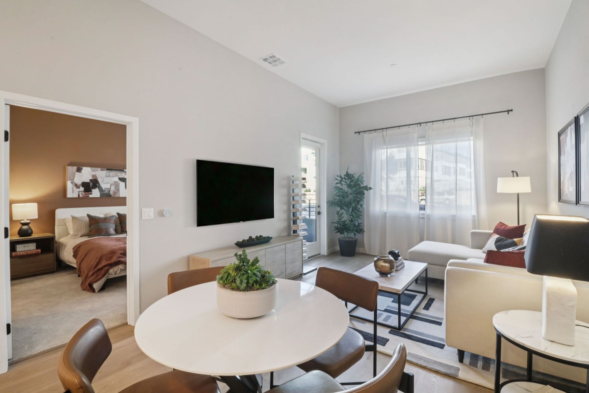 Living room with dining area, open to a bedroom; neutral tones, modern furniture.