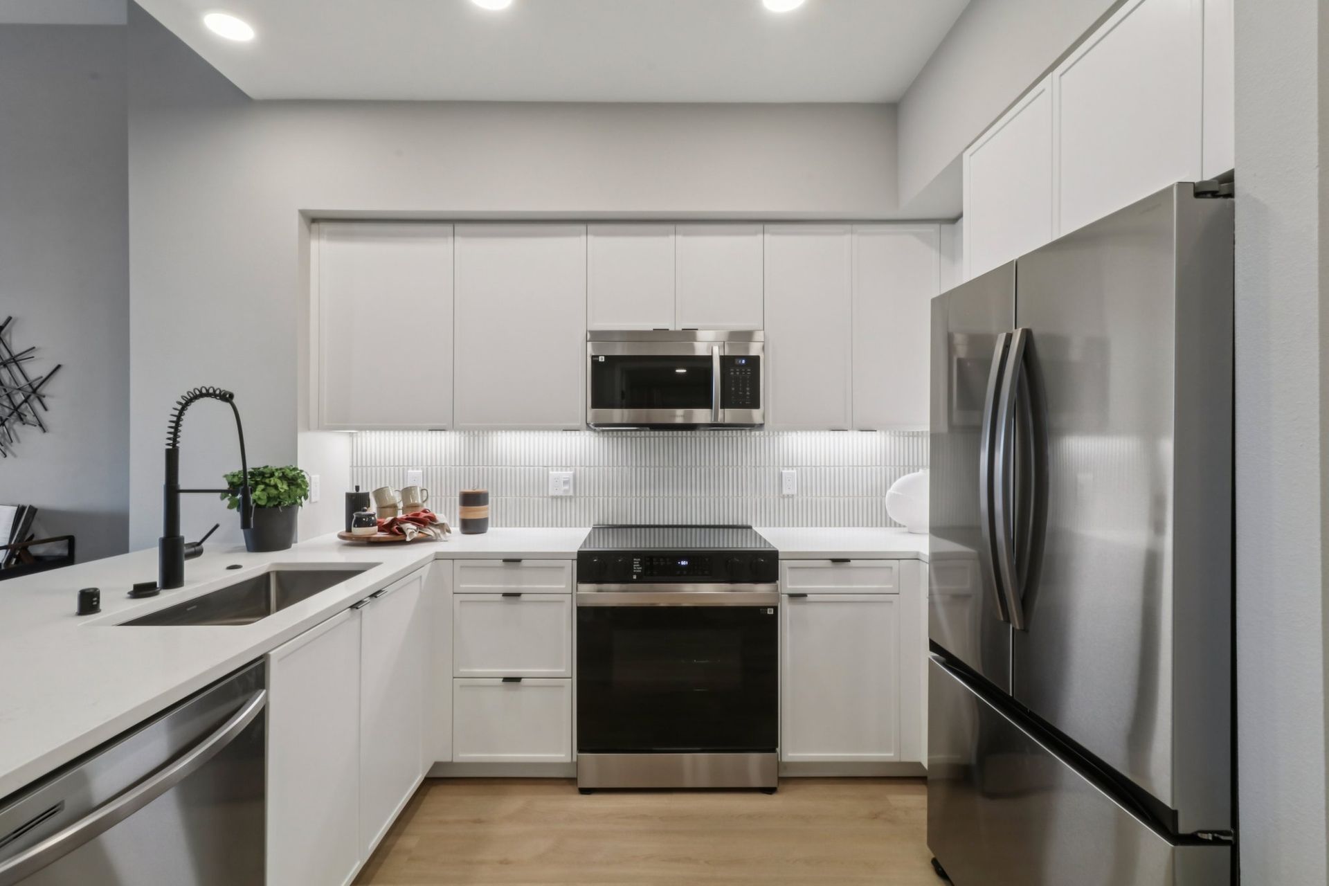 Modern kitchen with white cabinets, stainless steel appliances, and light wood flooring.