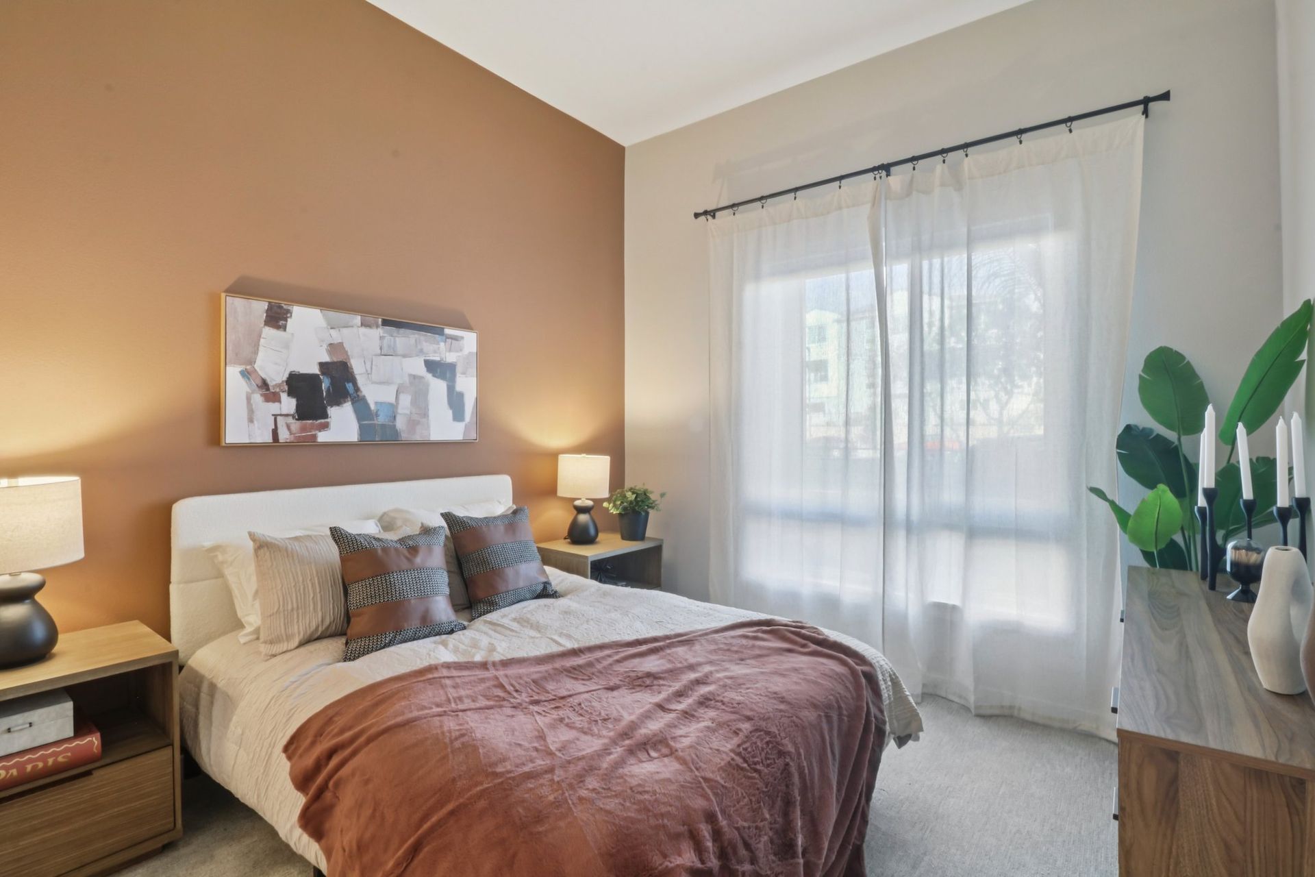 Bedroom with bed, nightstands, artwork, sheer curtains, and a brown accent wall.