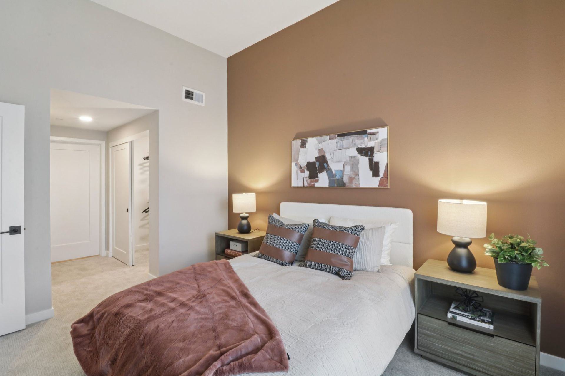 Bedroom with a bed, nightstands, lamps, artwork, and a brown accent wall.