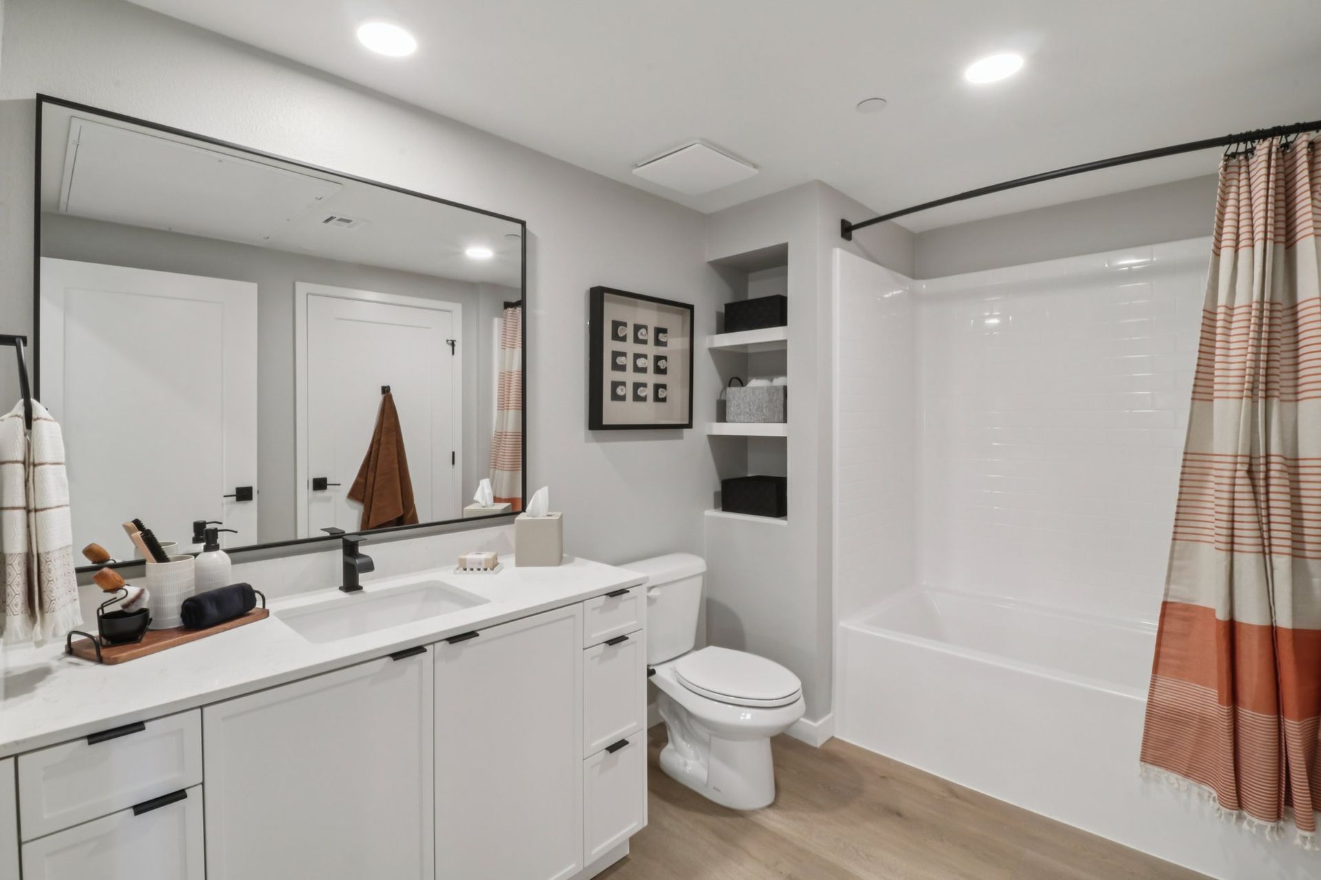 Modern bathroom with white vanity, large mirror, and a white bathtub with patterned shower curtain.
