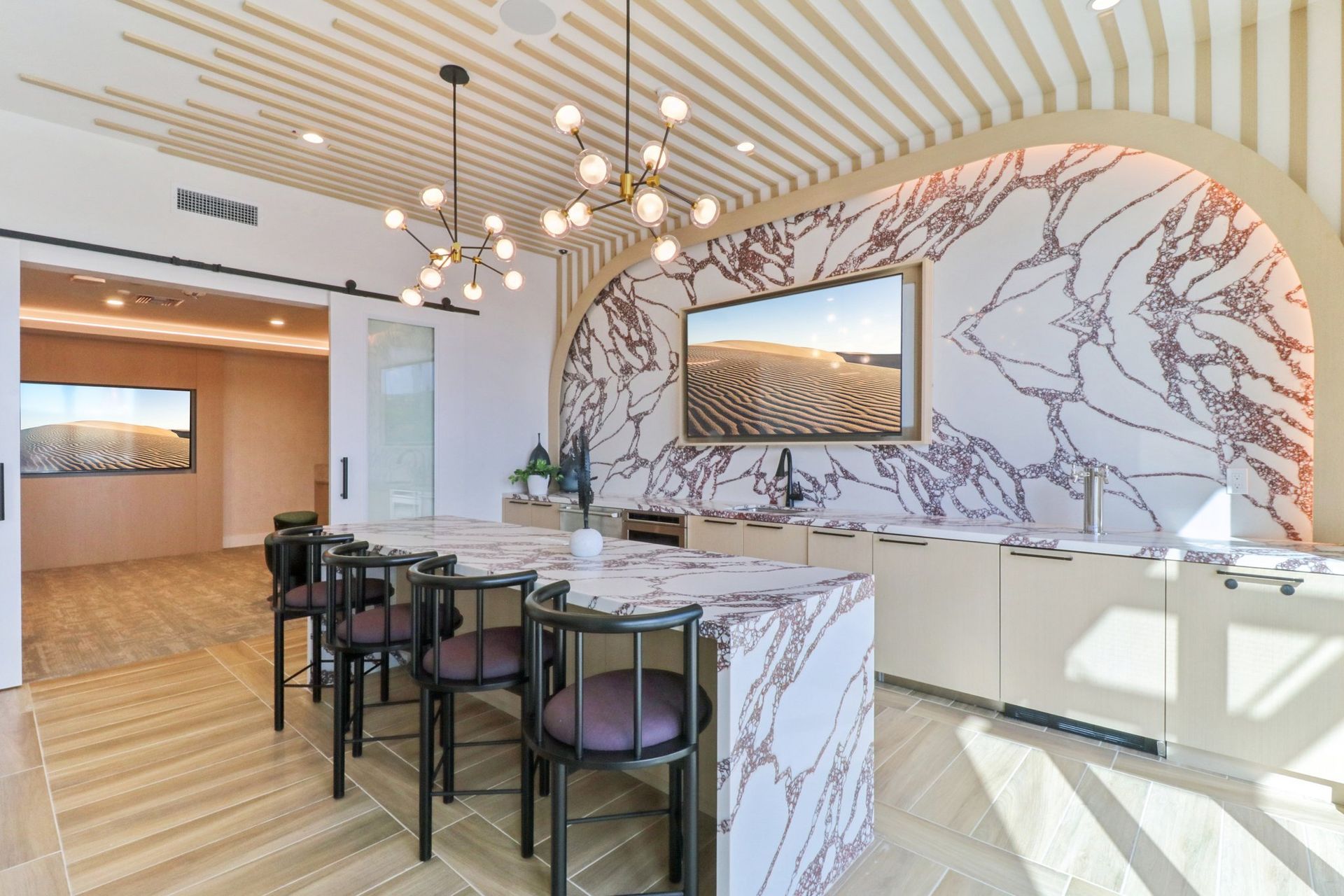 Modern kitchen with marble countertops, bar stools, and a TV; light wood floors and accent wall.
