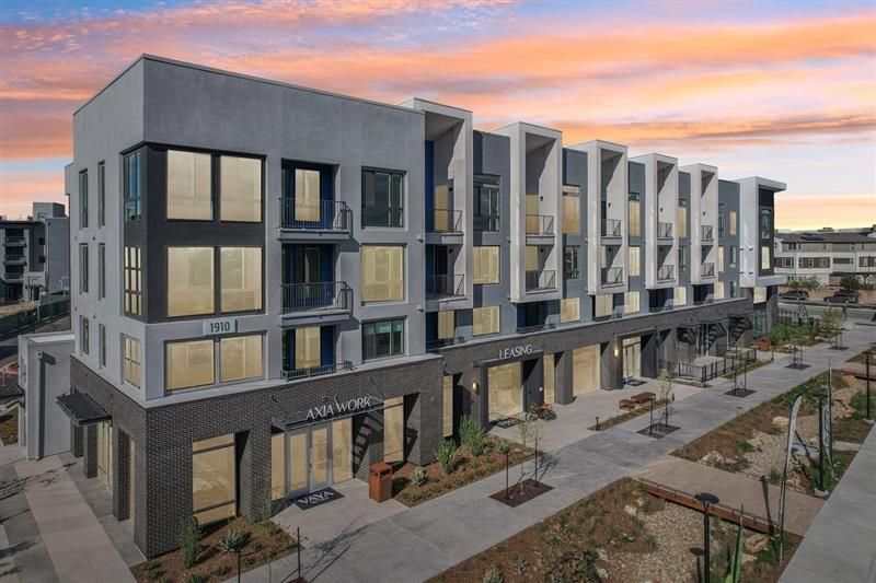 Modern multi-story building with storefronts at ground level; sunset sky in the background.