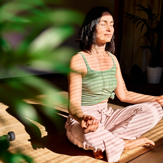 A woman is sitting in a lotus position with her eyes closed.