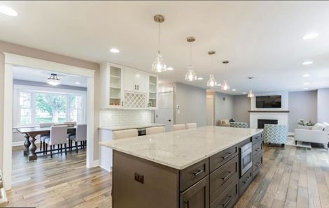 A living room with a chandelier hanging from the ceiling and a kitchen in the background.