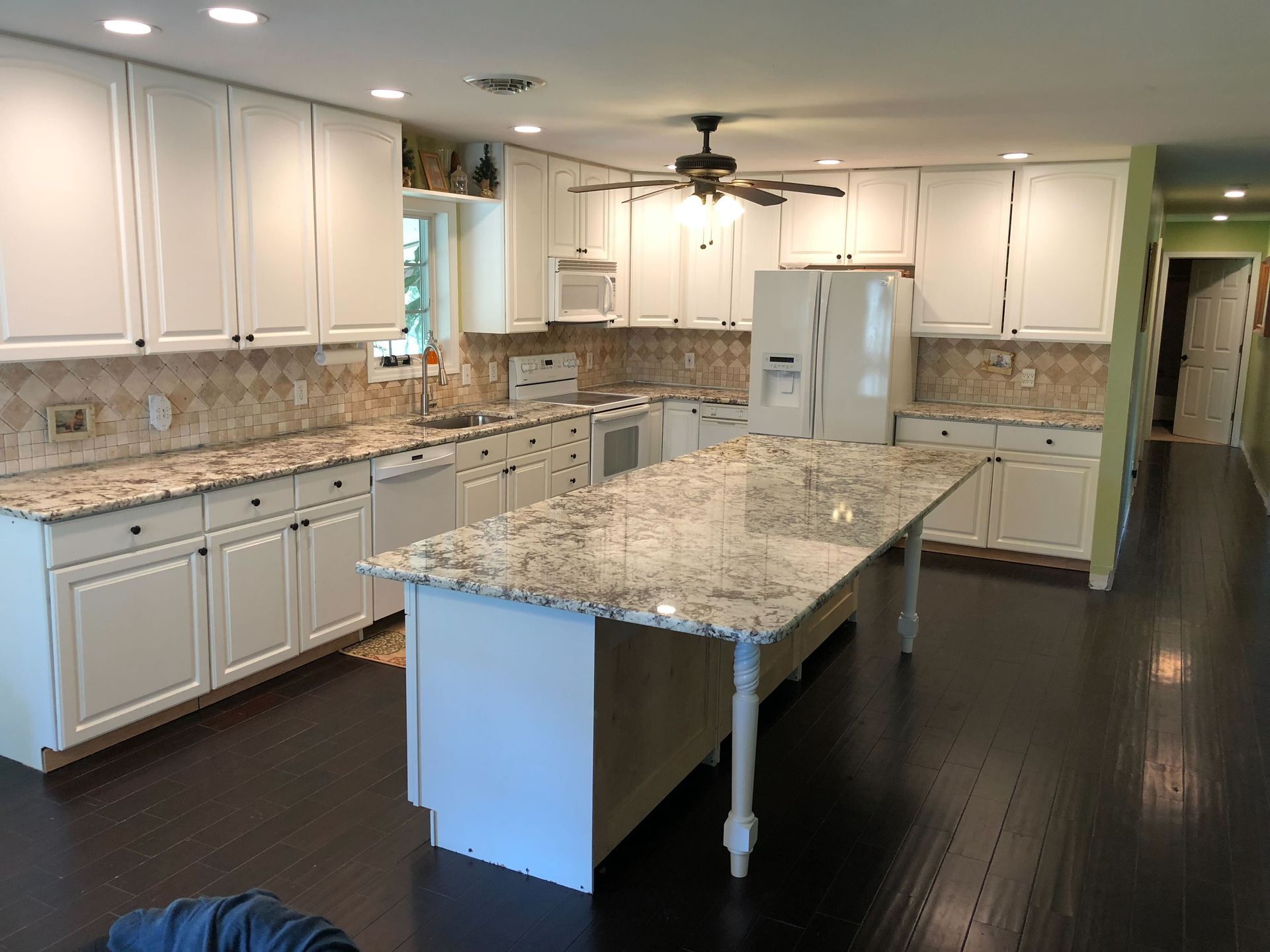 A living room with a chandelier hanging from the ceiling and a kitchen in the background.