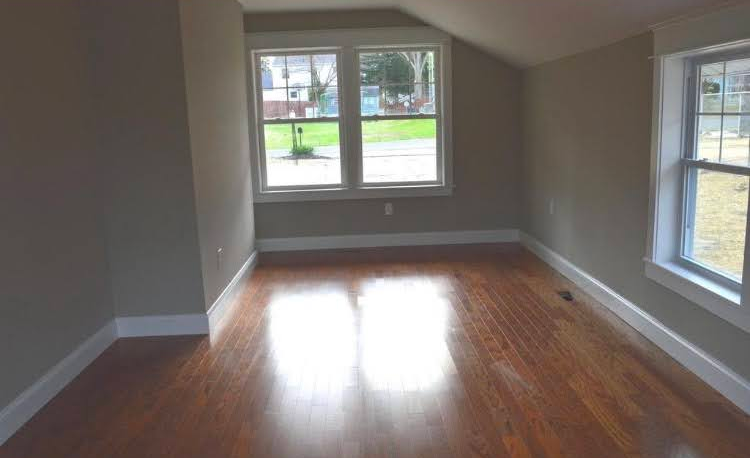 An empty room with hardwood floors and two windows.