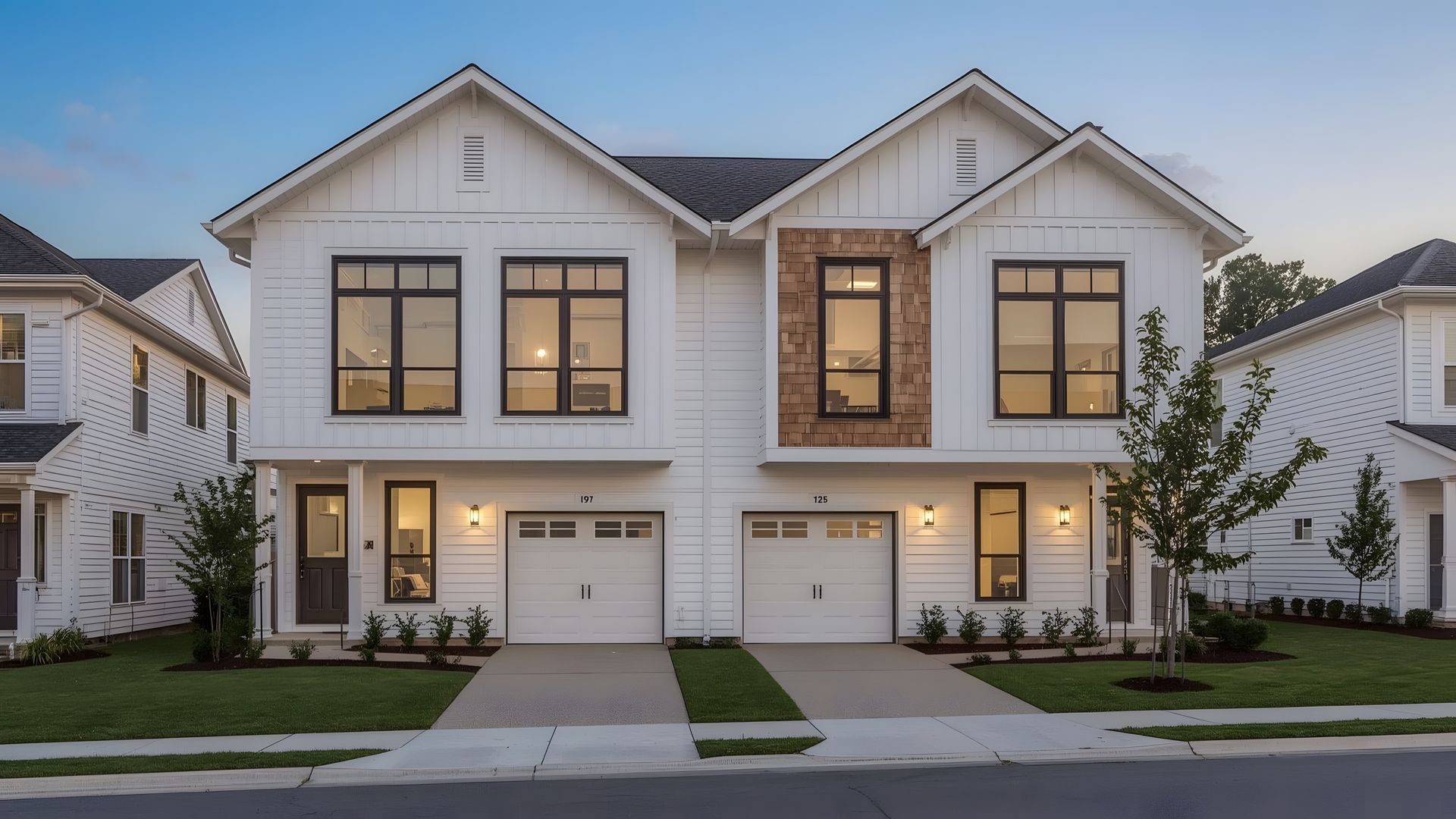 White modern duplex with two-car garages, black framed windows, and a stone accent between units.