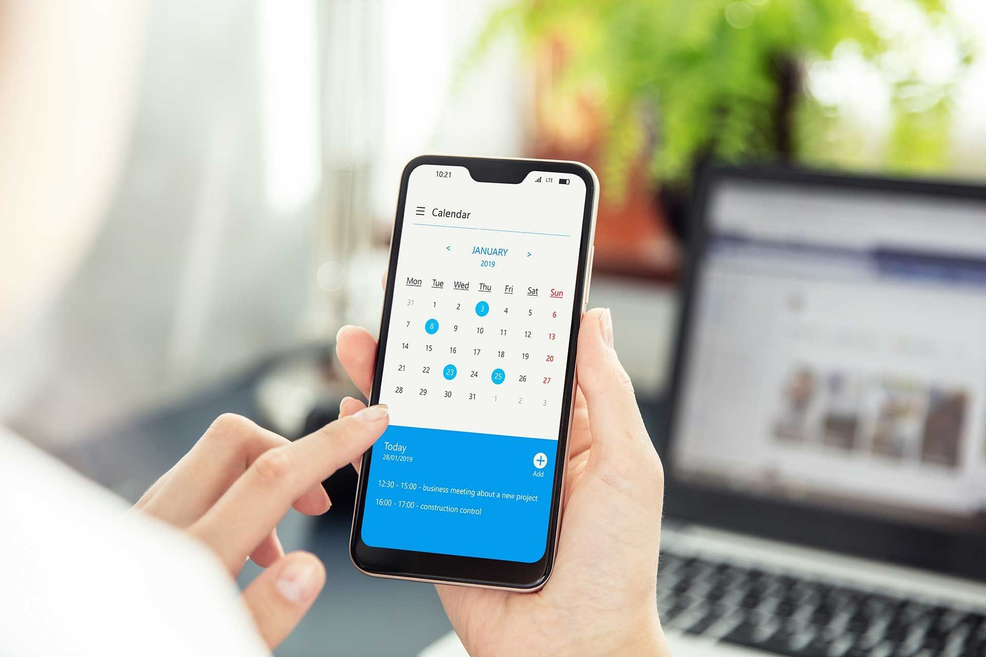 A person is holding a cell phone in front of a laptop.