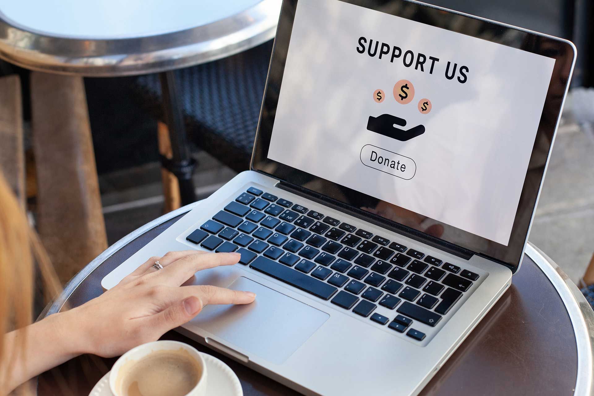 A person is using a laptop computer with the words support us on the screen.