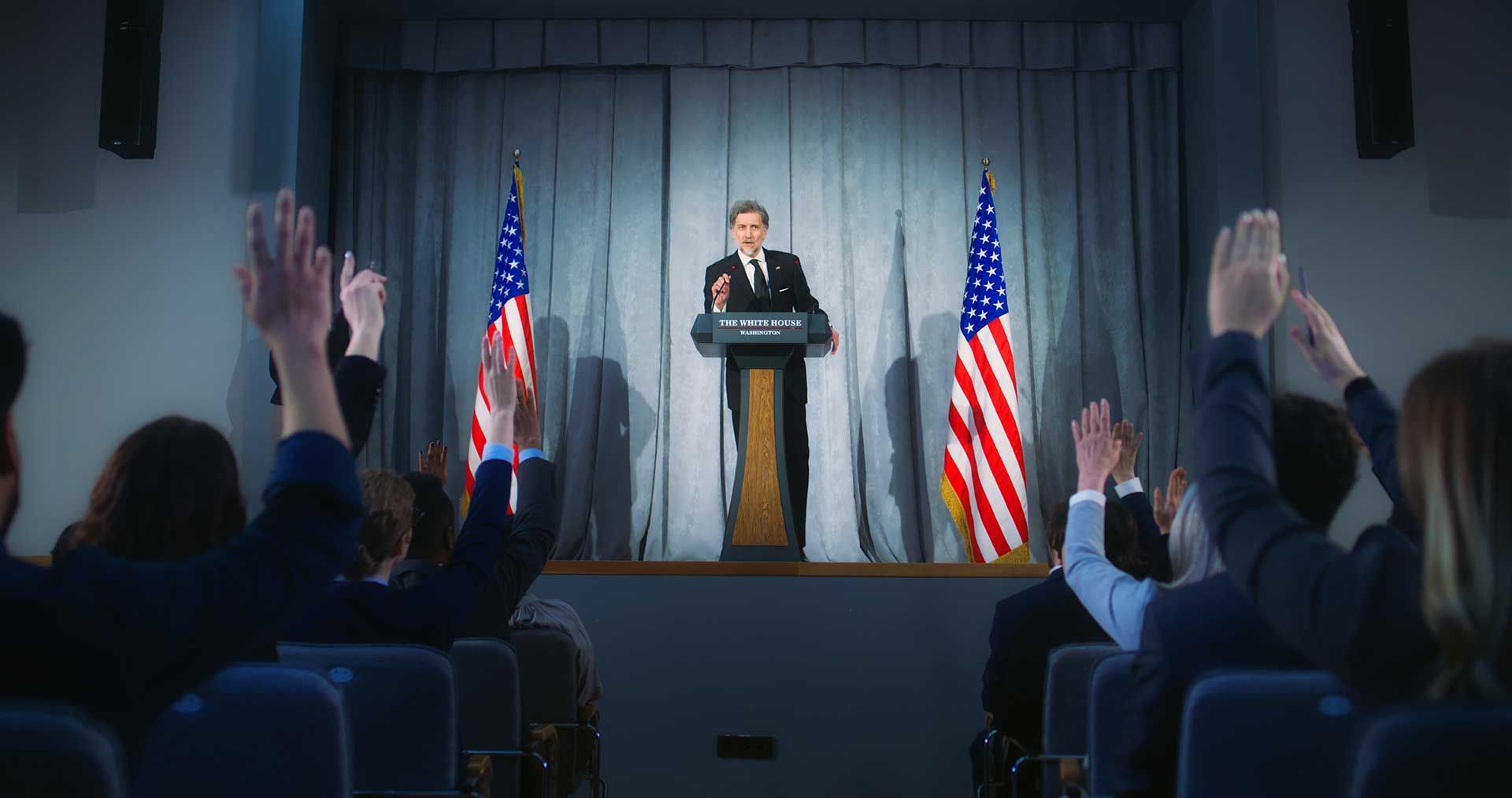 A man is giving a speech at a podium in front of a crowd of people.