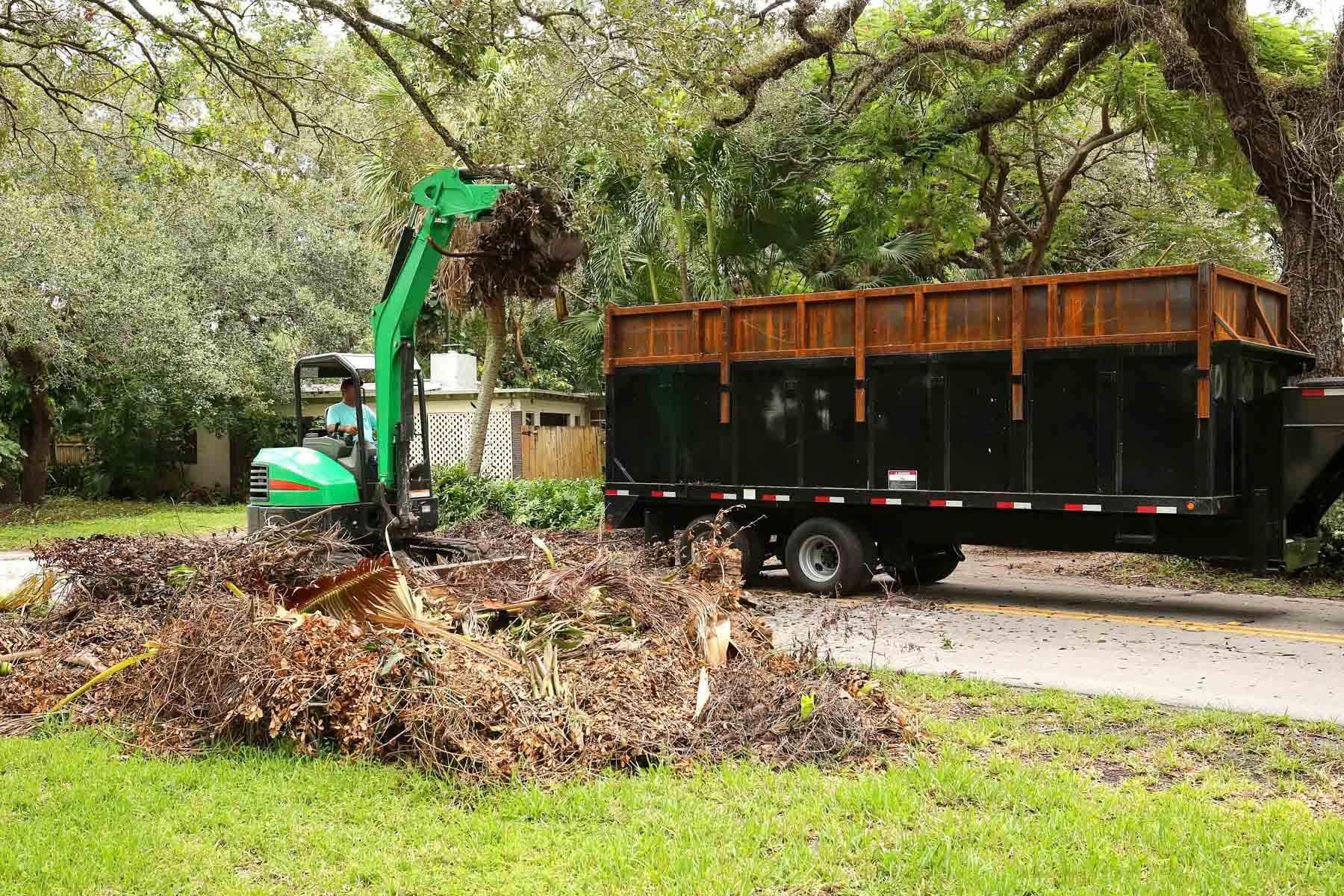 A small green excavator loading debris into a trailer on a residential street.