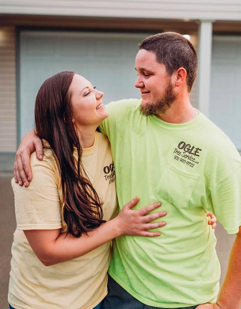 Woman in yellow shirt, man in green shirt smiling at each other, arms around each other.