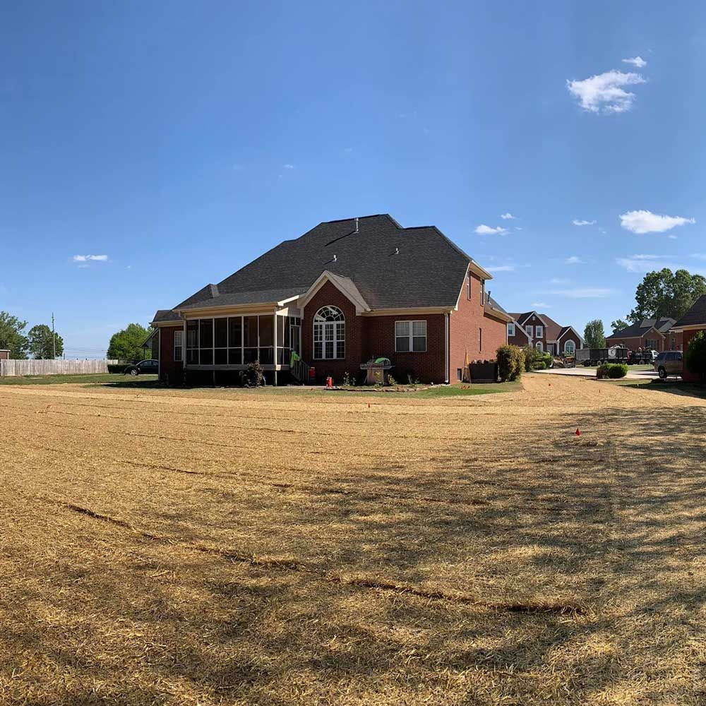 Red brick house with a dark roof and a large, dry lawn under a blue sky.