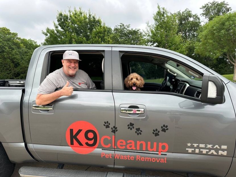 A man is sitting in the back of a truck with a dog in the window.