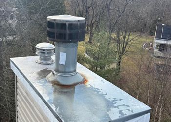 A chimney on the roof of a house with trees in the background.