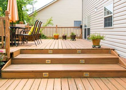 A wooden deck with stairs leading up to it in front of a house.