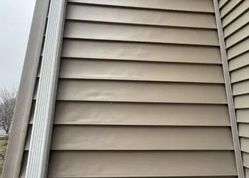 A close up of a tan siding on a house with a white trim.