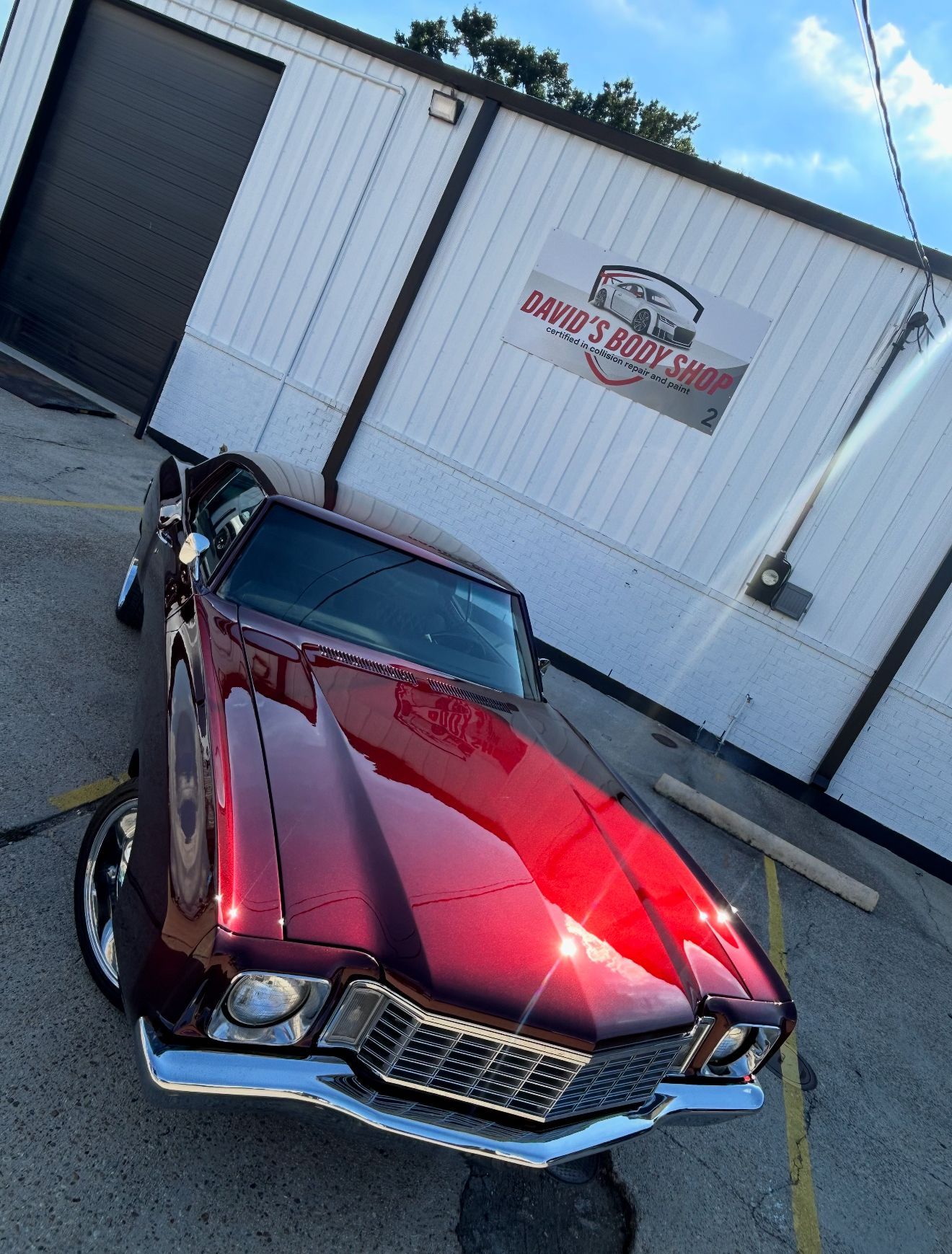 Red classic car parked outside a shop with a sign.