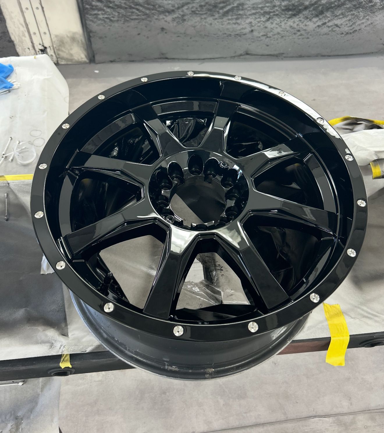 Black alloy wheel with a shiny finish, on a gray surface.