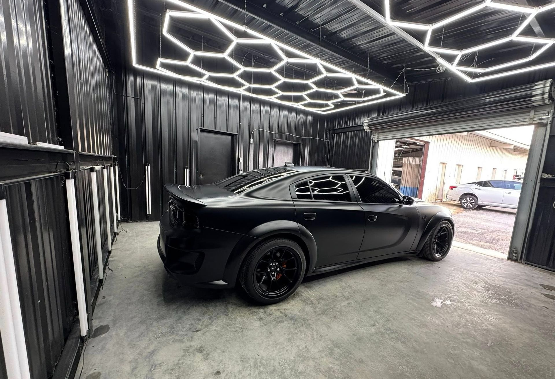 Black Dodge Charger in a black garage with honeycomb lights.