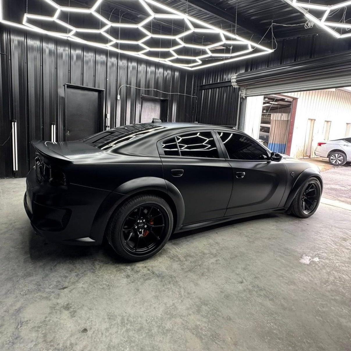Black matte Dodge Charger in a garage with honeycomb lighting.