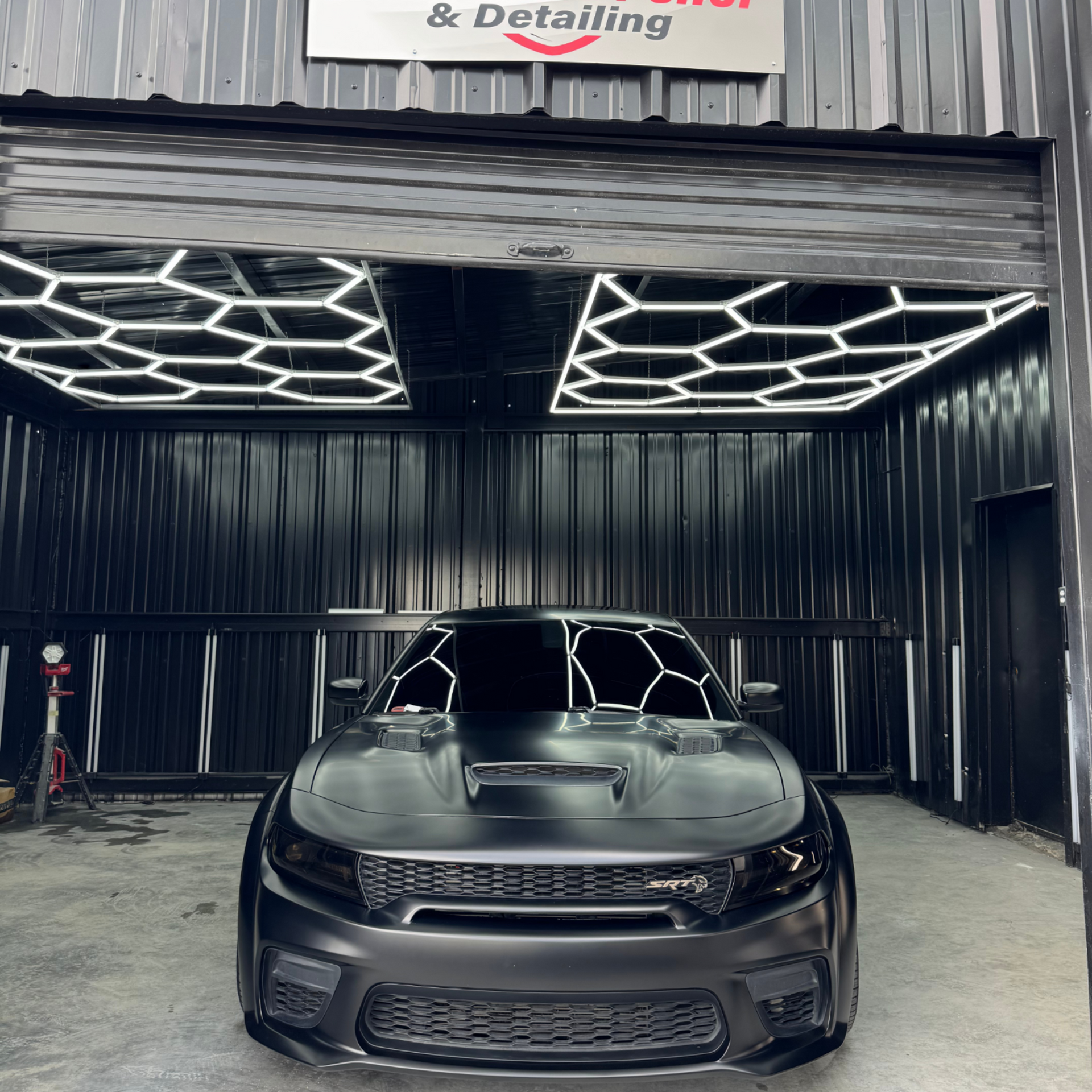 Black Dodge Charger inside a car detailing shop, illuminated by hexagonal lights.
