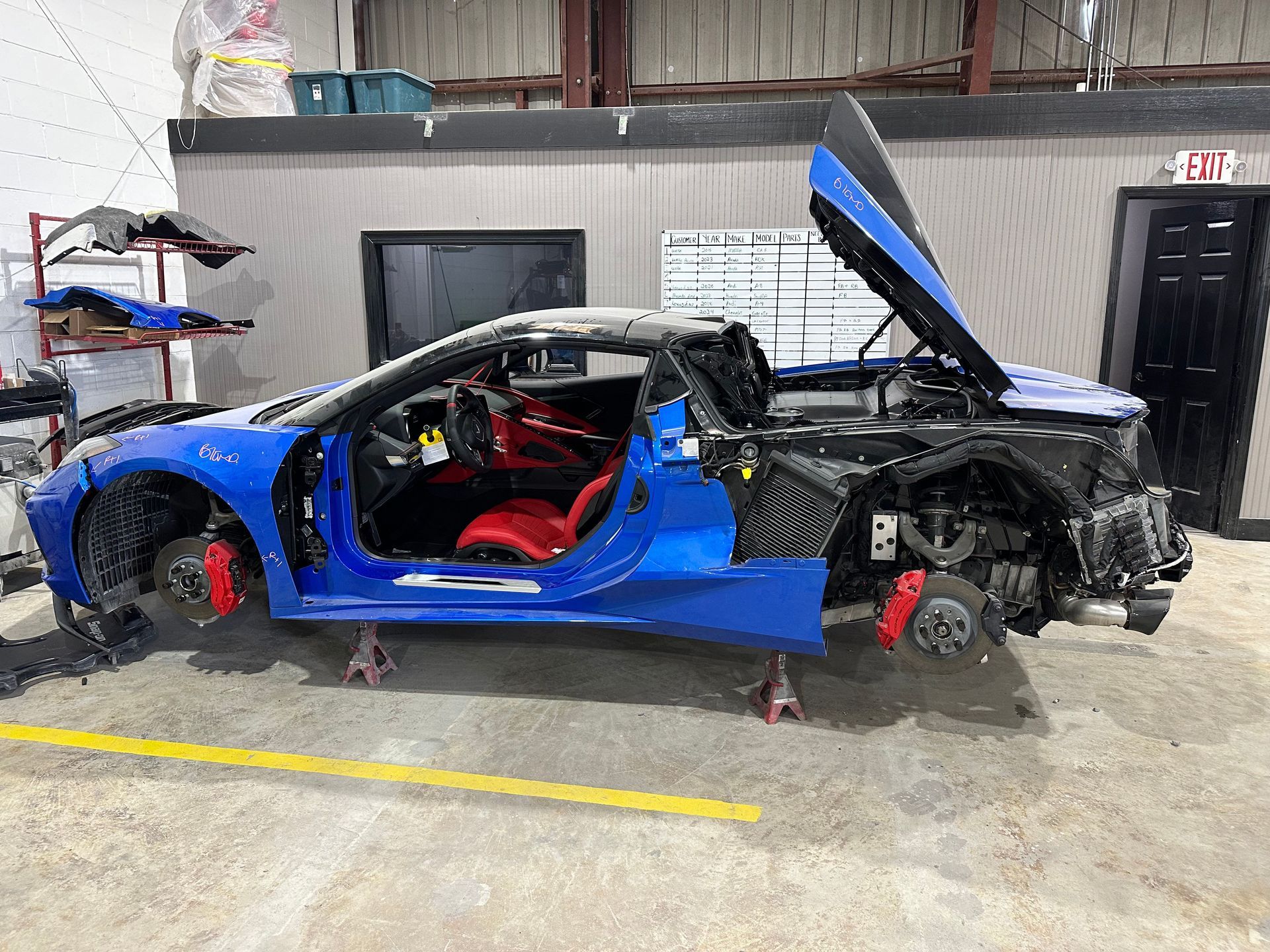 Blue Corvette convertible being worked on in a garage. Car is partially disassembled. Red seats and brake calipers.