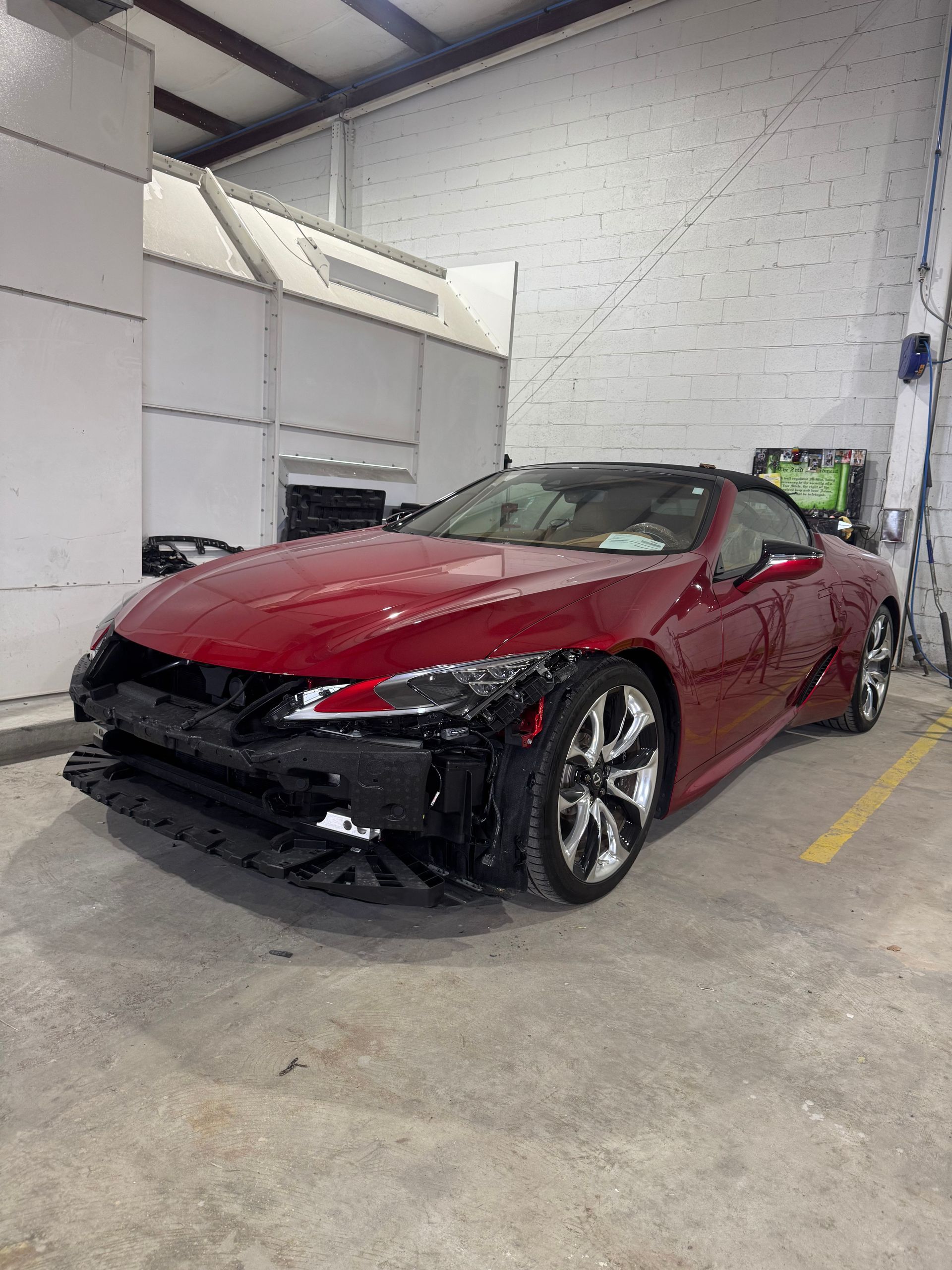 Red Lexus LC convertible in a repair shop with front bumper damage.