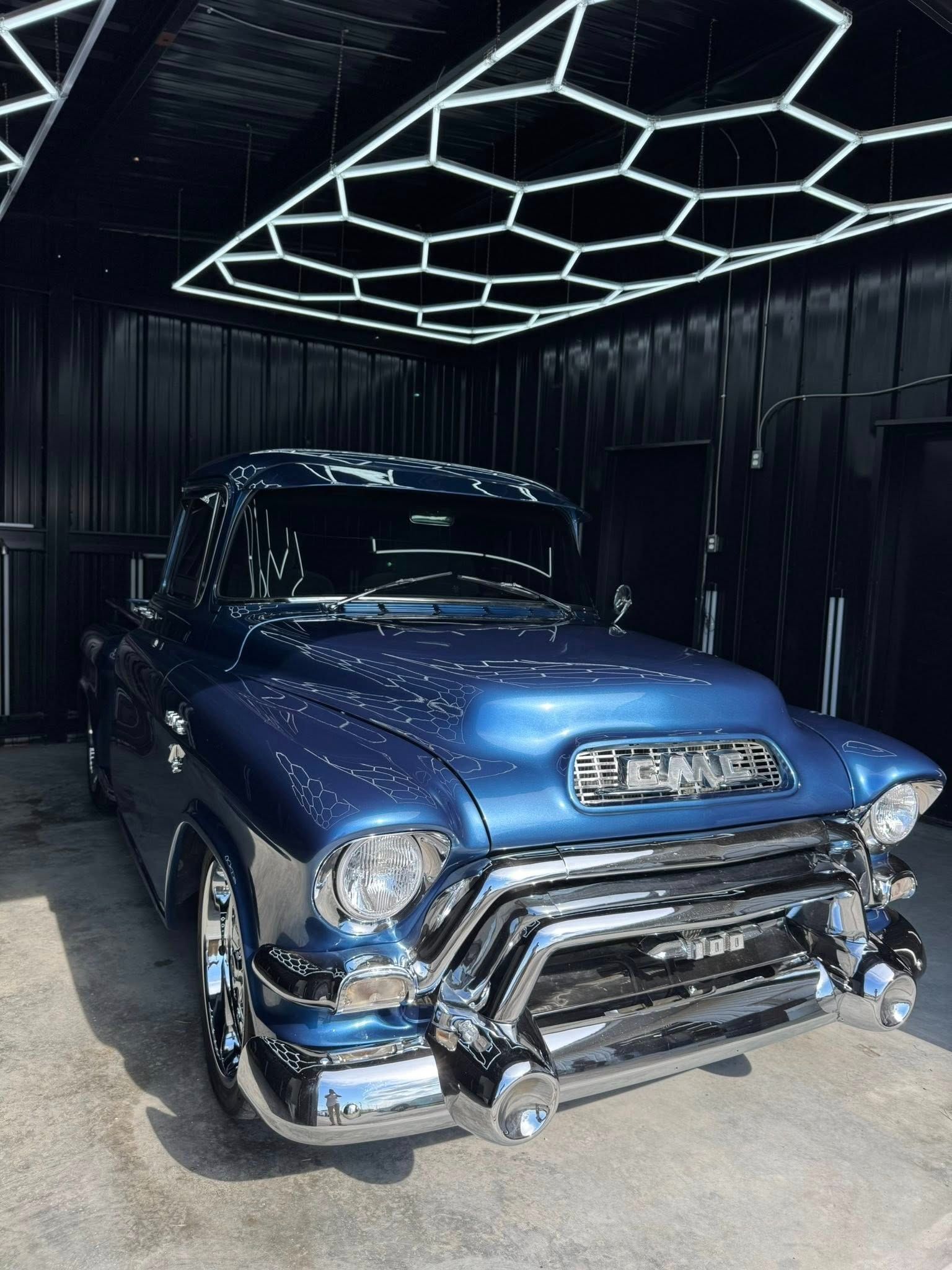 Blue vintage GMC truck in a garage with chrome detailing and a honeycomb ceiling light.