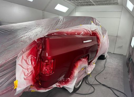 Truck bed in a paint booth, partially masked and freshly painted a vibrant red.