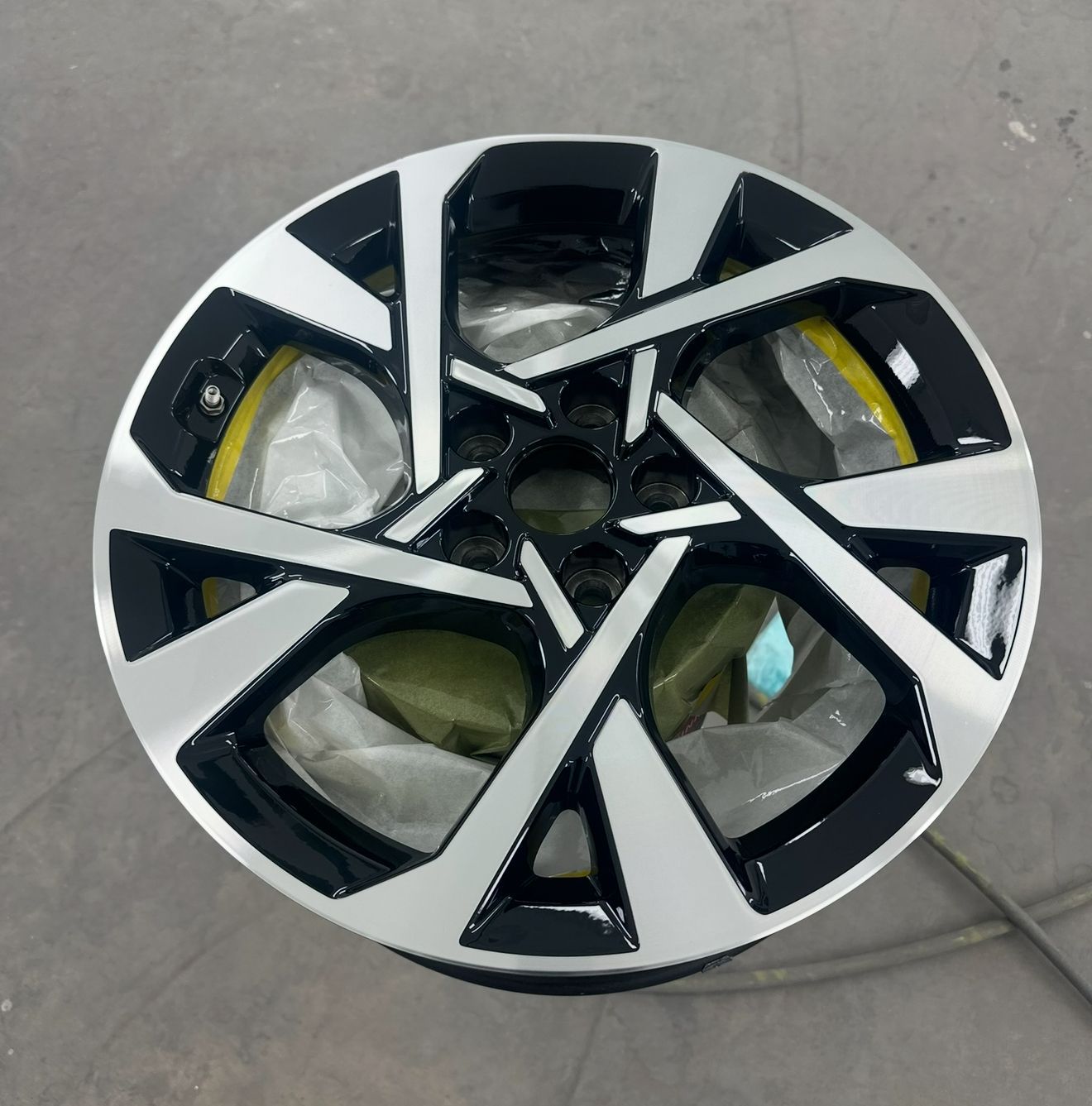 Car wheel with black and silver design, mounted on a gray surface.