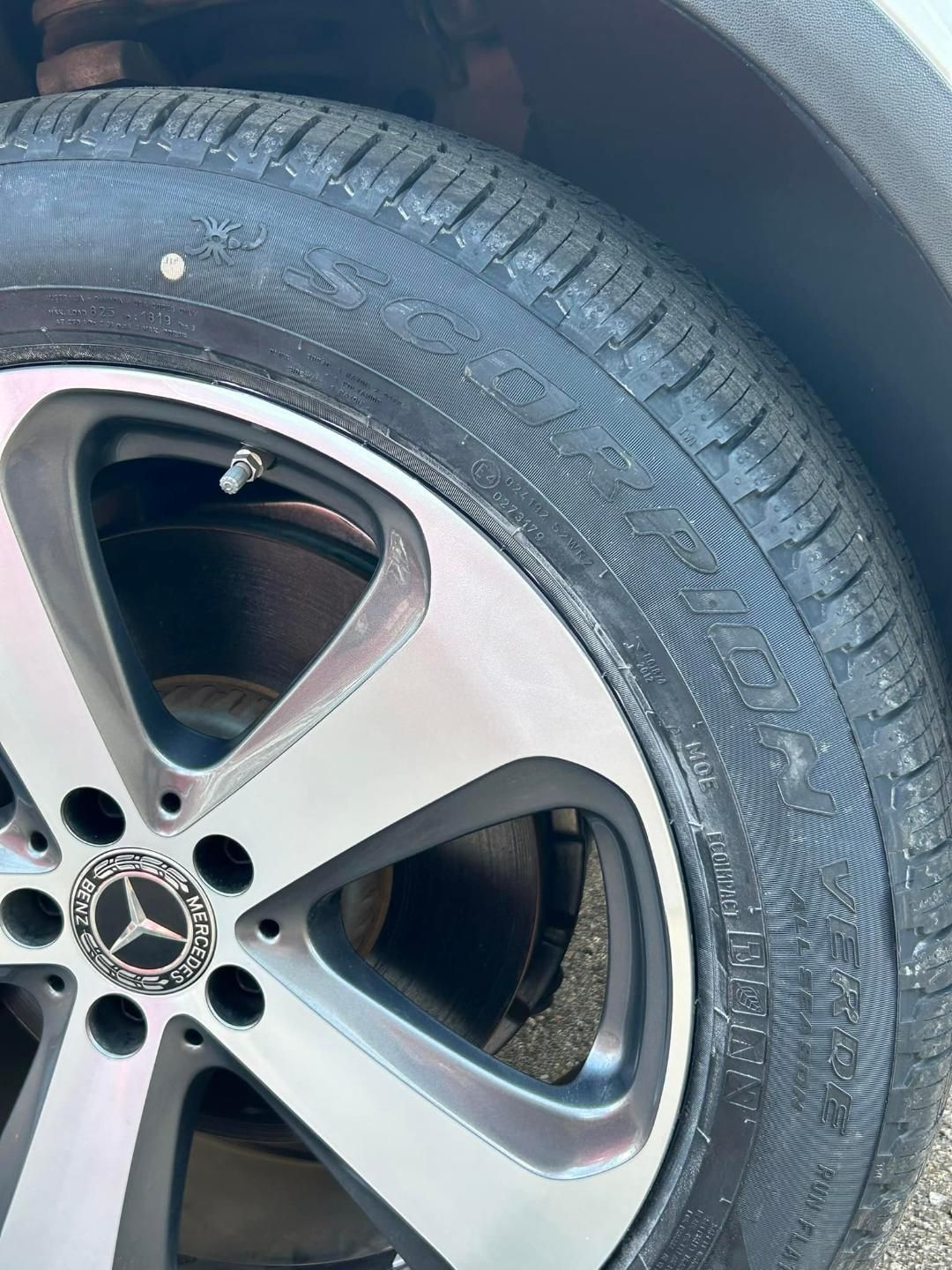 Close-up of a car tire on a Mercedes-Benz alloy wheel, with a nail embedded in the tire tread.