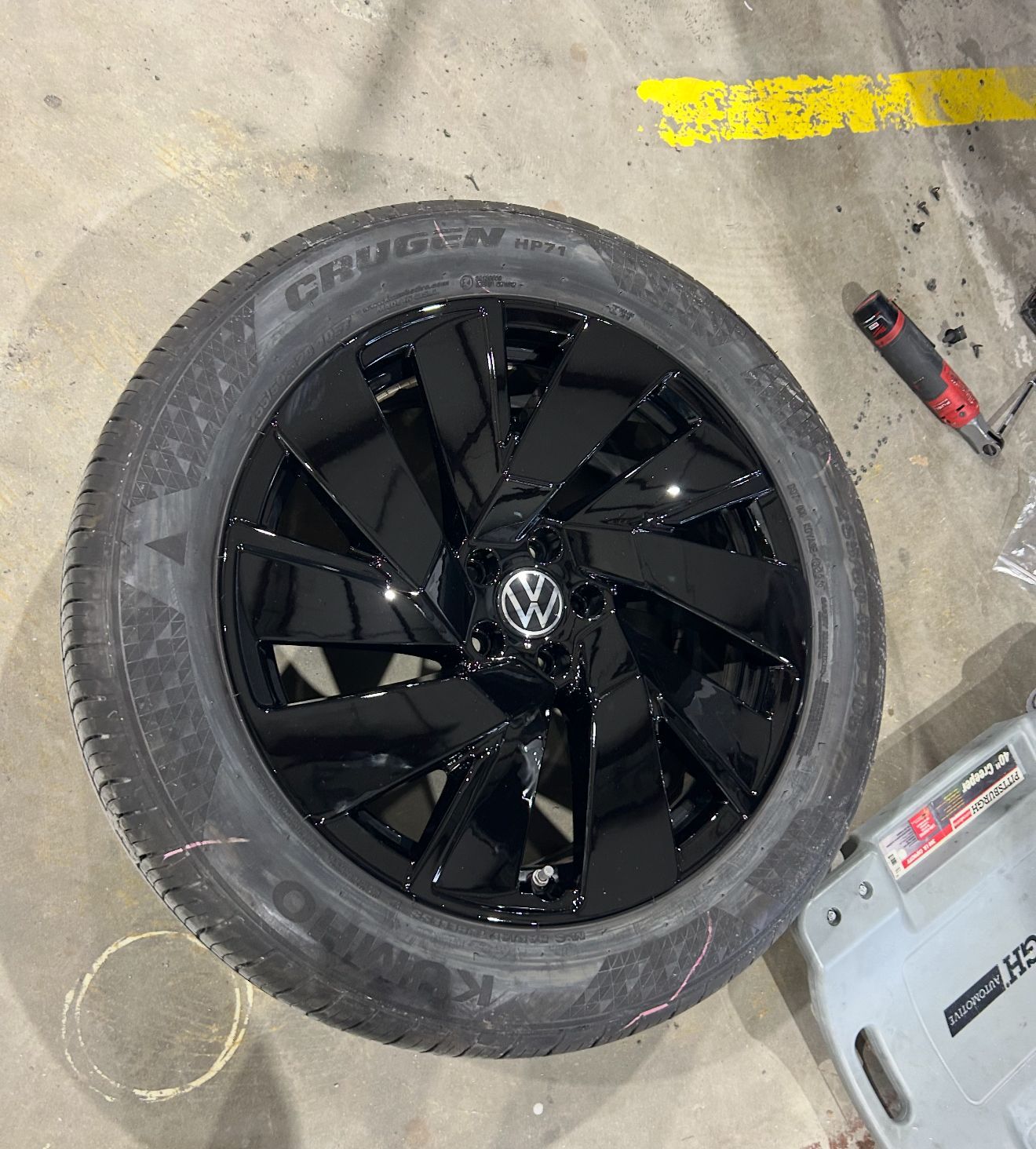 Black Volkswagen wheel with tire on a concrete floor.
