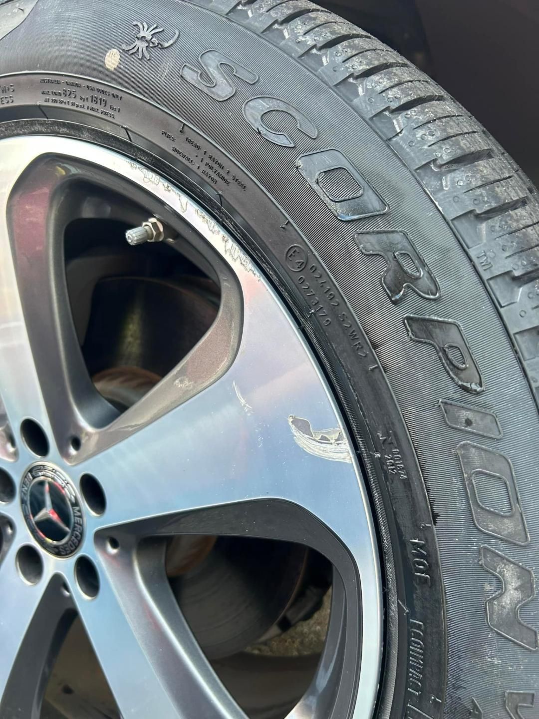 Close-up of a silver Mercedes-Benz rim with tire, showing minor scratches and the brand name on tire.