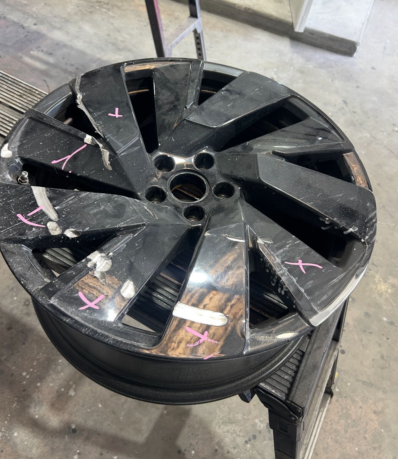 Damaged black car wheel on a shop floor, with many cracks and pink markings.