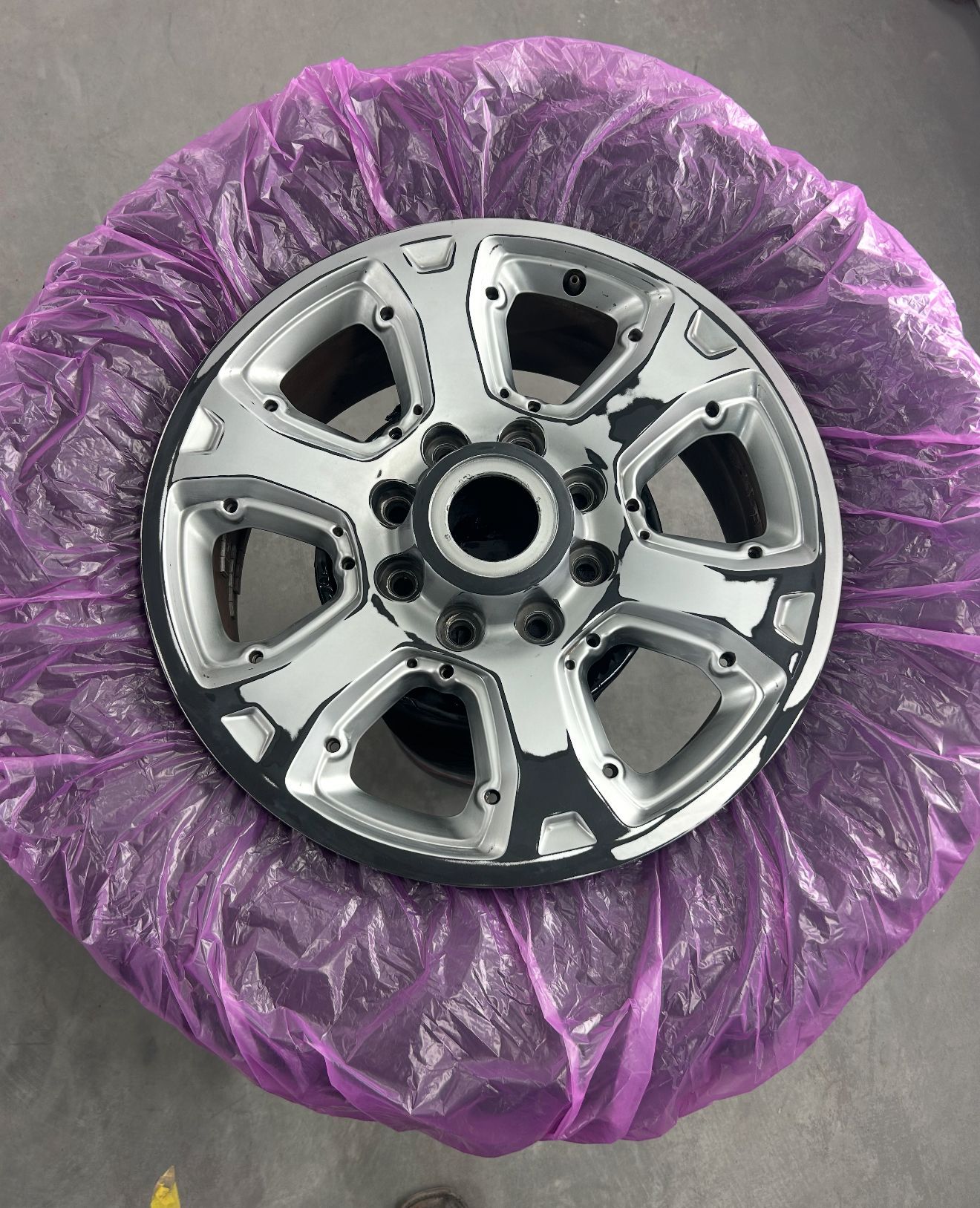 Silver car wheel wrapped in purple protective plastic.