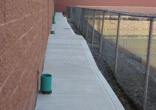 A concrete walkway next to a chain link fence and a brick wall