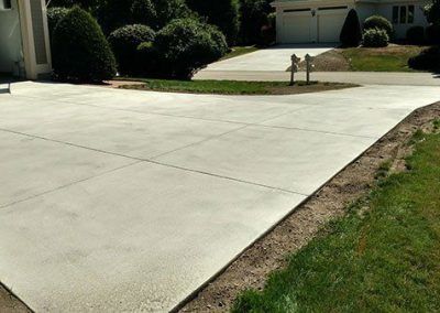 A concrete driveway leading to a house with a fire hydrant in the middle of it.