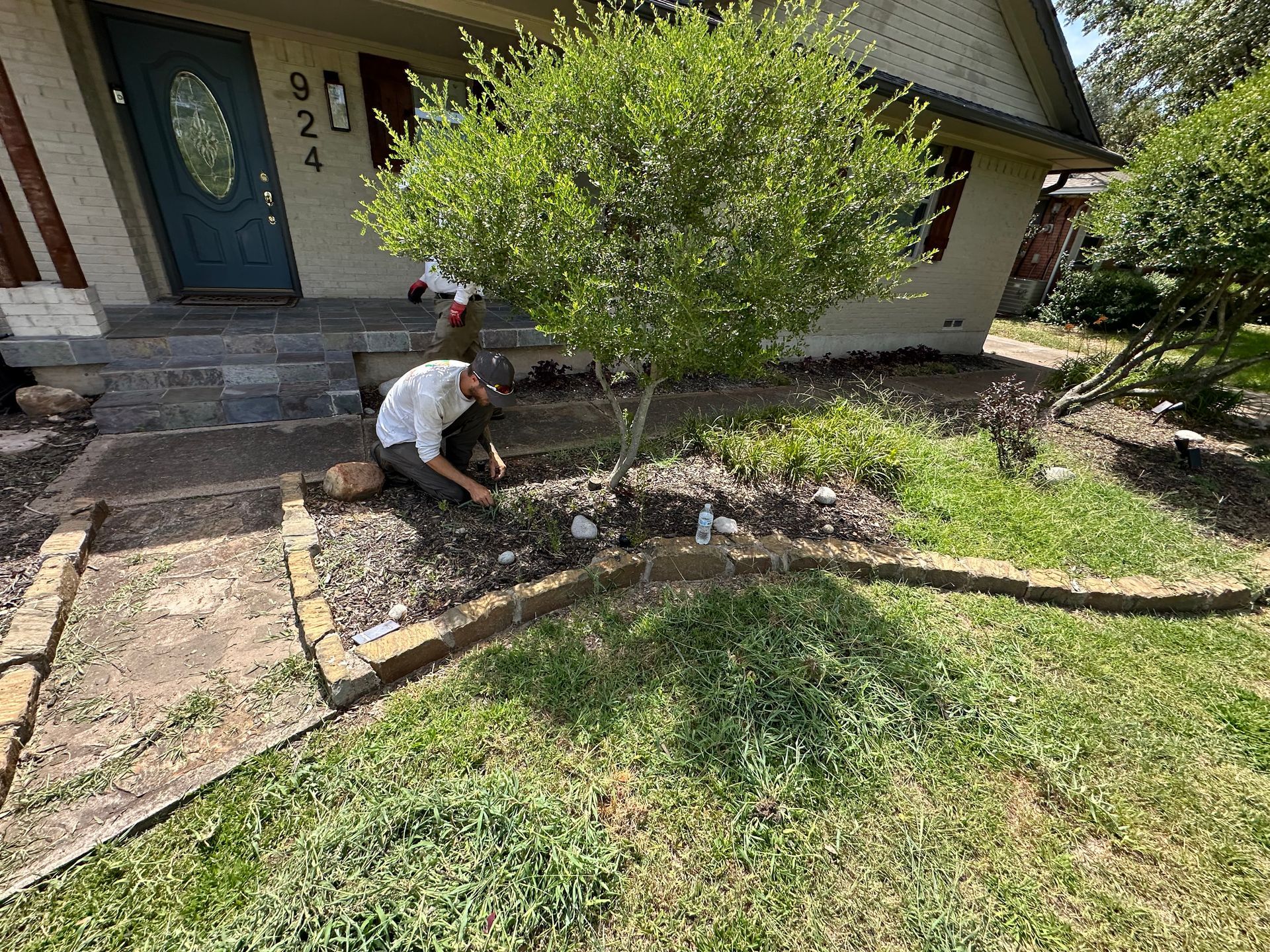 A man is kneeling down in a garden in front of a house.