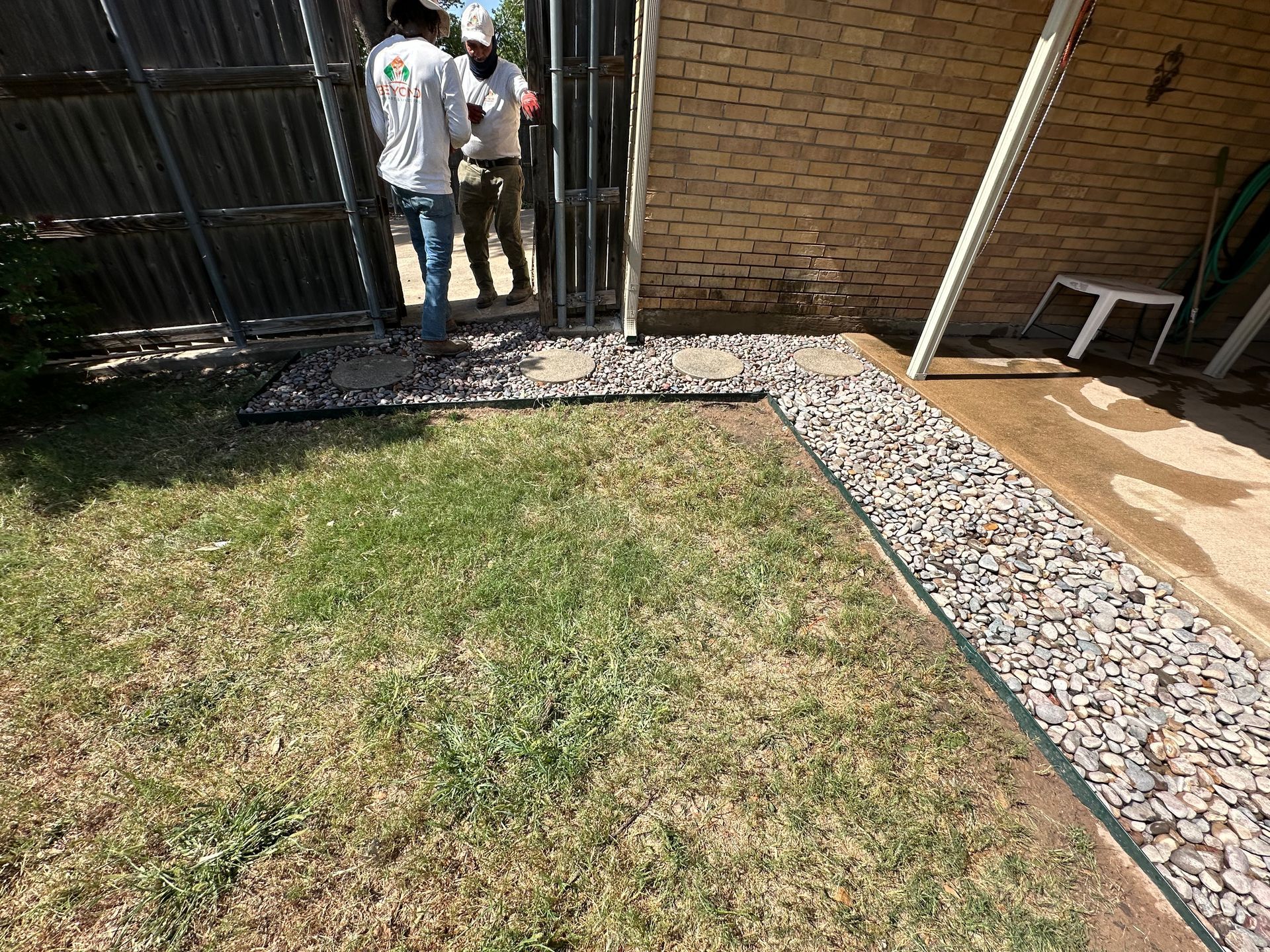 A couple of people standing in front of a fence in a yard.