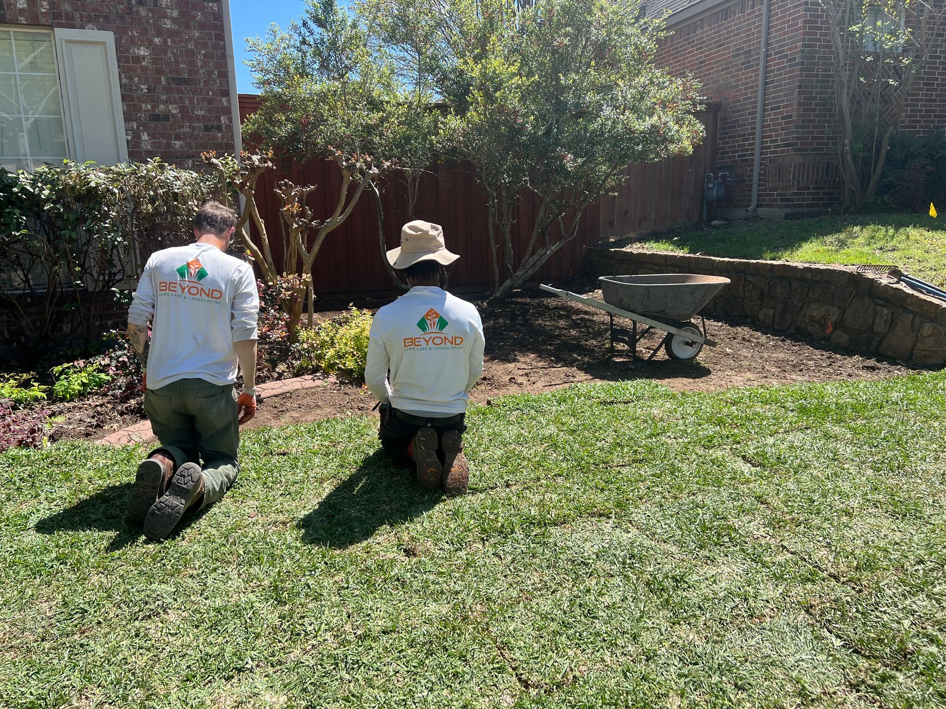 Two men are kneeling on the grass in a backyard.
