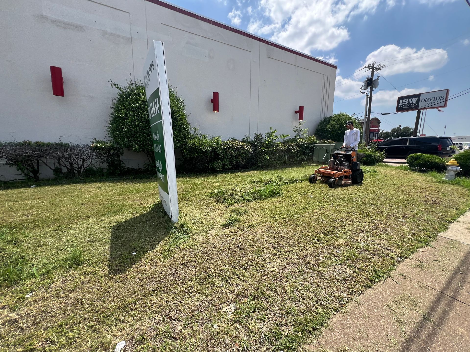 A man is mowing a lawn in front of a building.