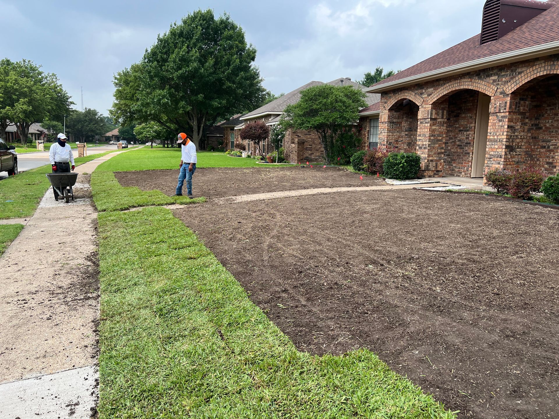 A man is pushing a wheelbarrow in front of a house.