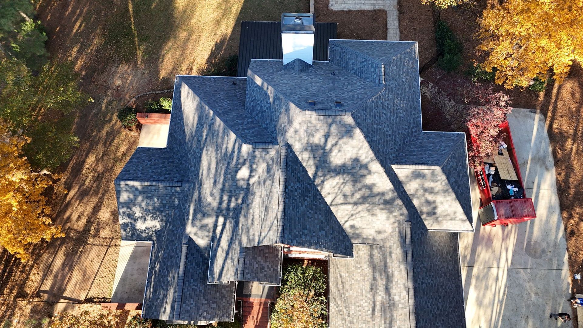 Overhead view of a house with a complex shingled roof, trees, and a driveway with a truck.