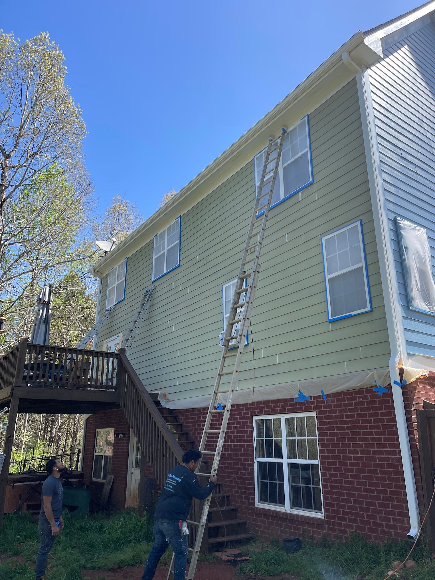 A man is painting the side of a house with a ladder.