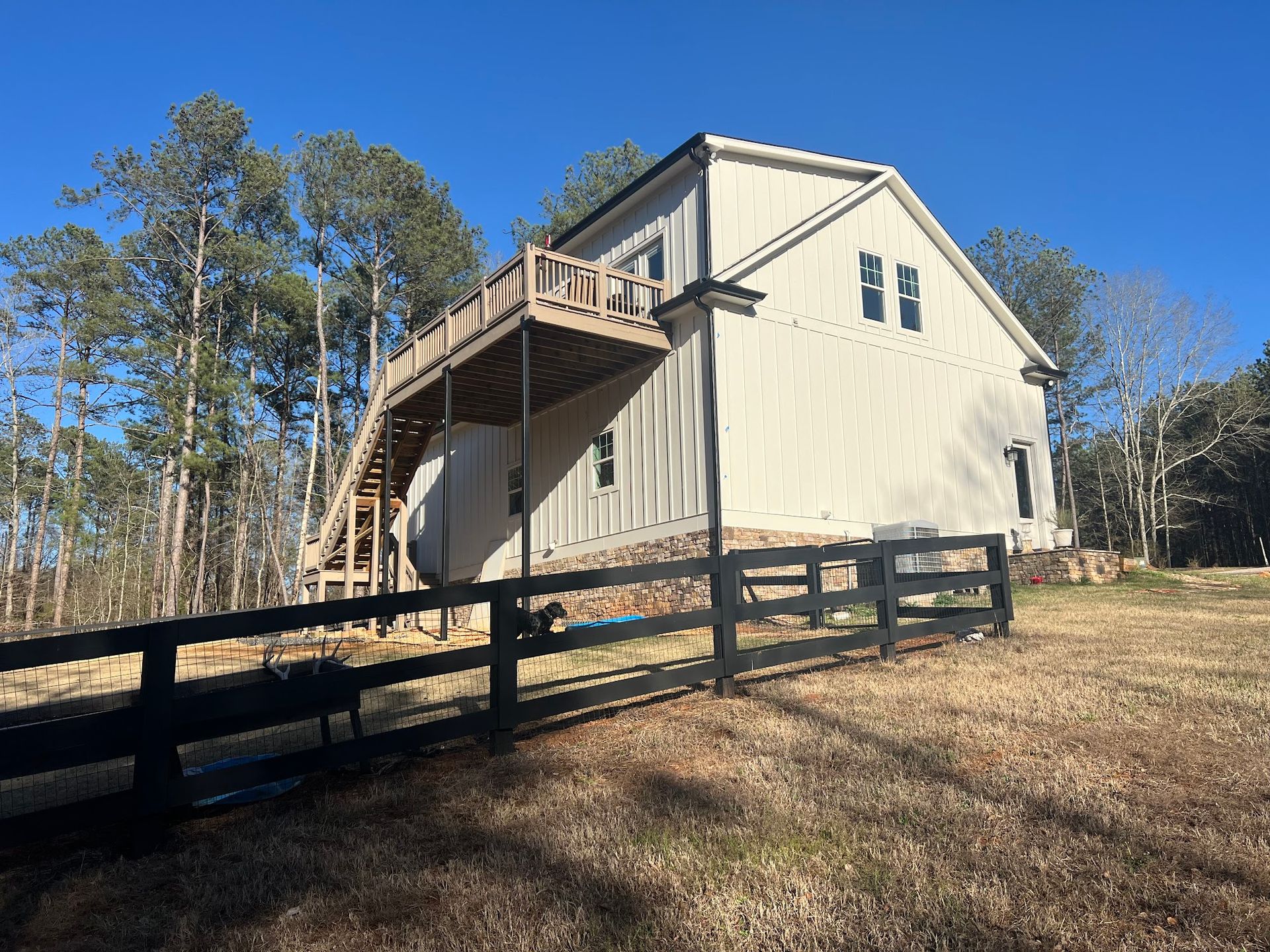 A white house with a wooden deck and a fence in front of it.