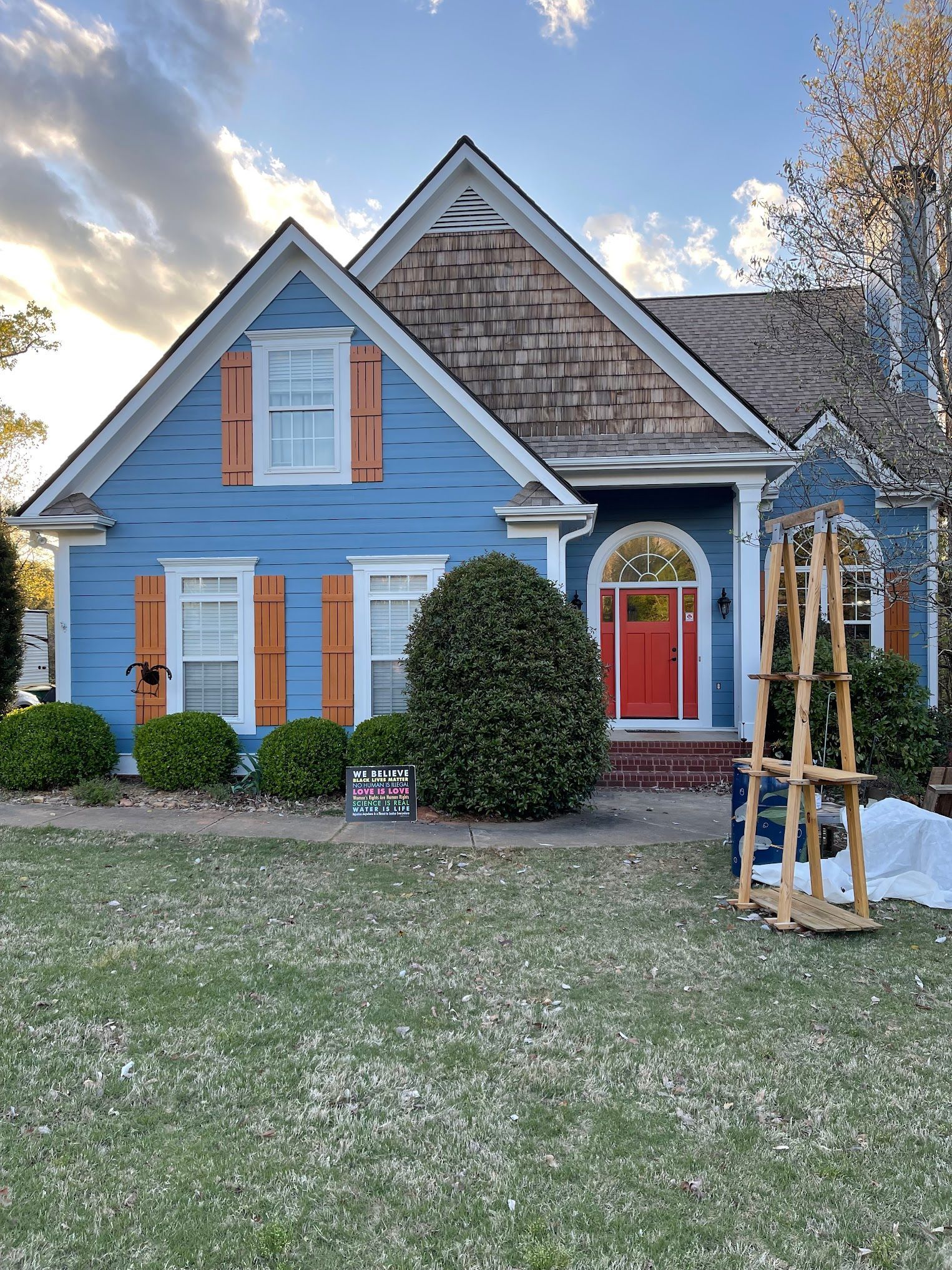A blue house with orange shutters and a red door is being painted.
