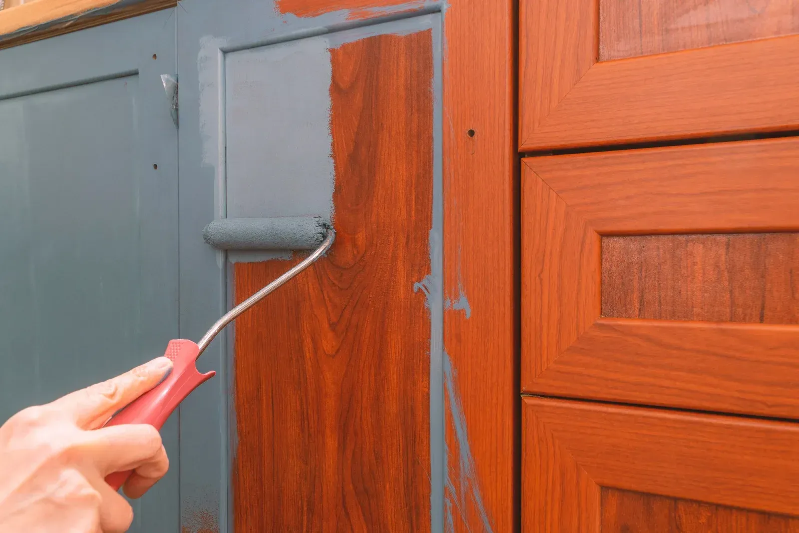 A person is painting a wooden cabinet with a roller.