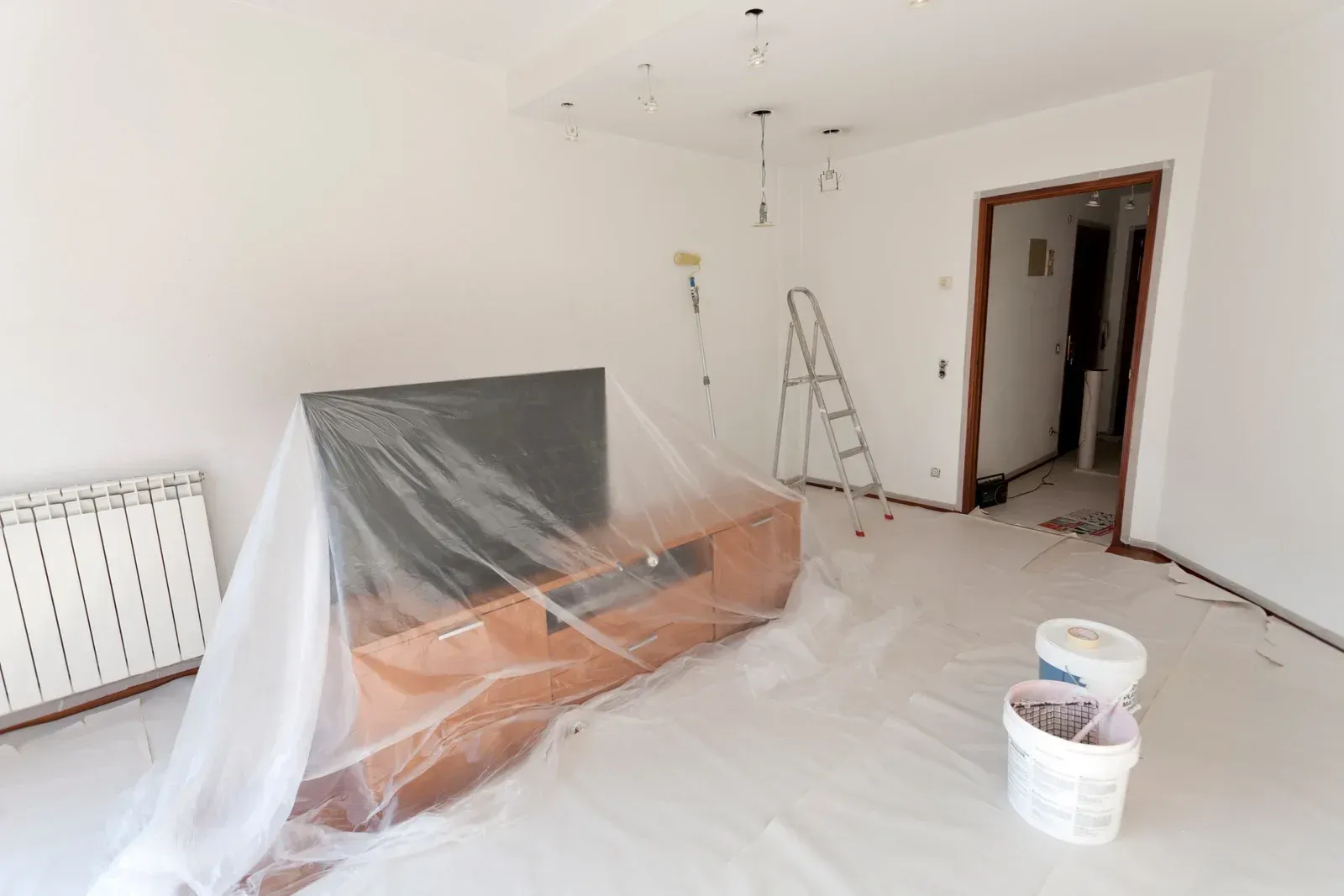 A living room is being painted and covered in plastic.